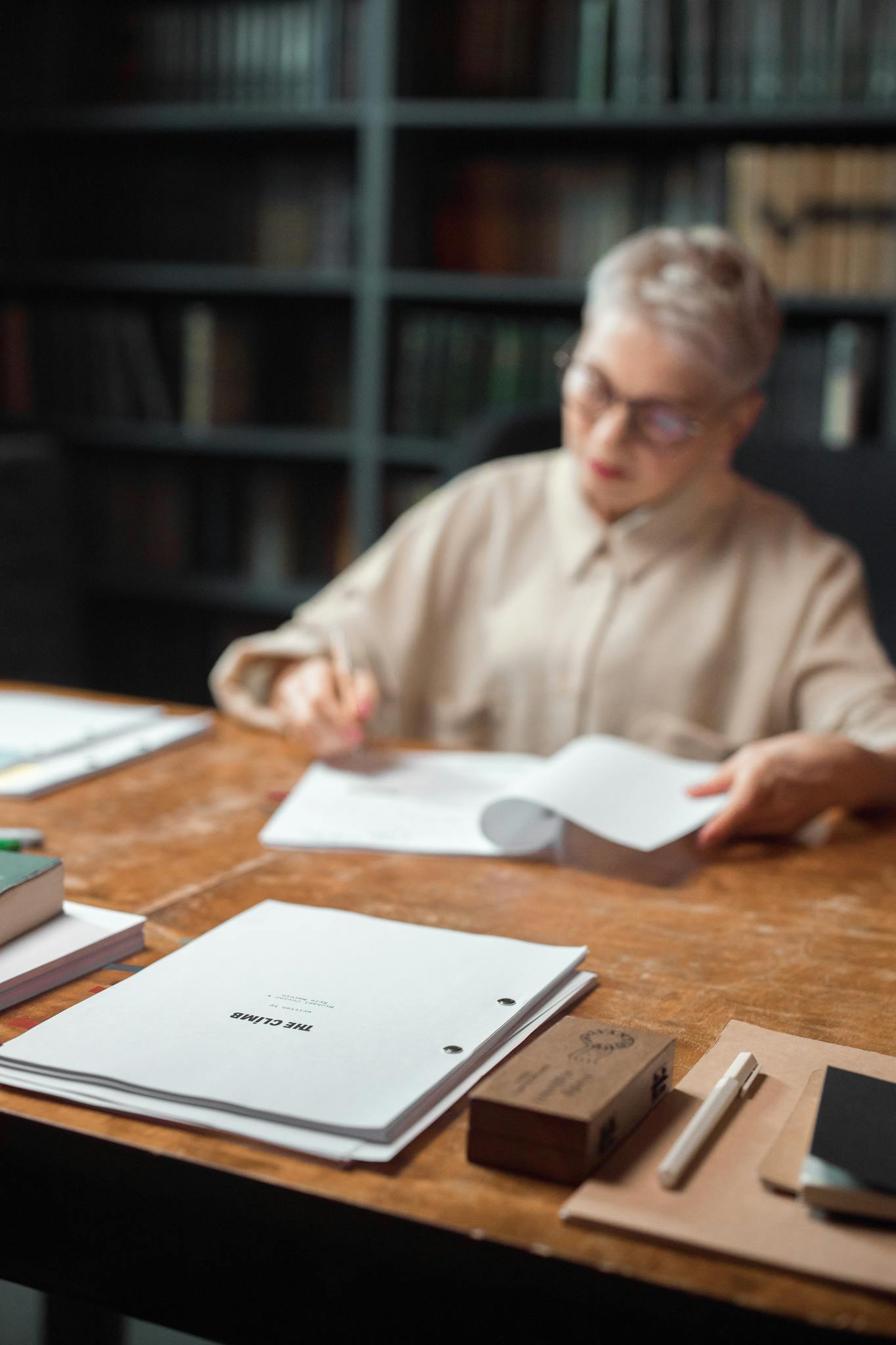 An editor is focused on reviewing and editing manuscripts at a wooden office table filled with papers.